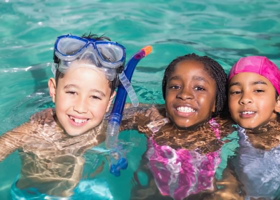 Three Children wearing swimsuits and snorkels in the outdoor pool at The Bethel Resort & Suites