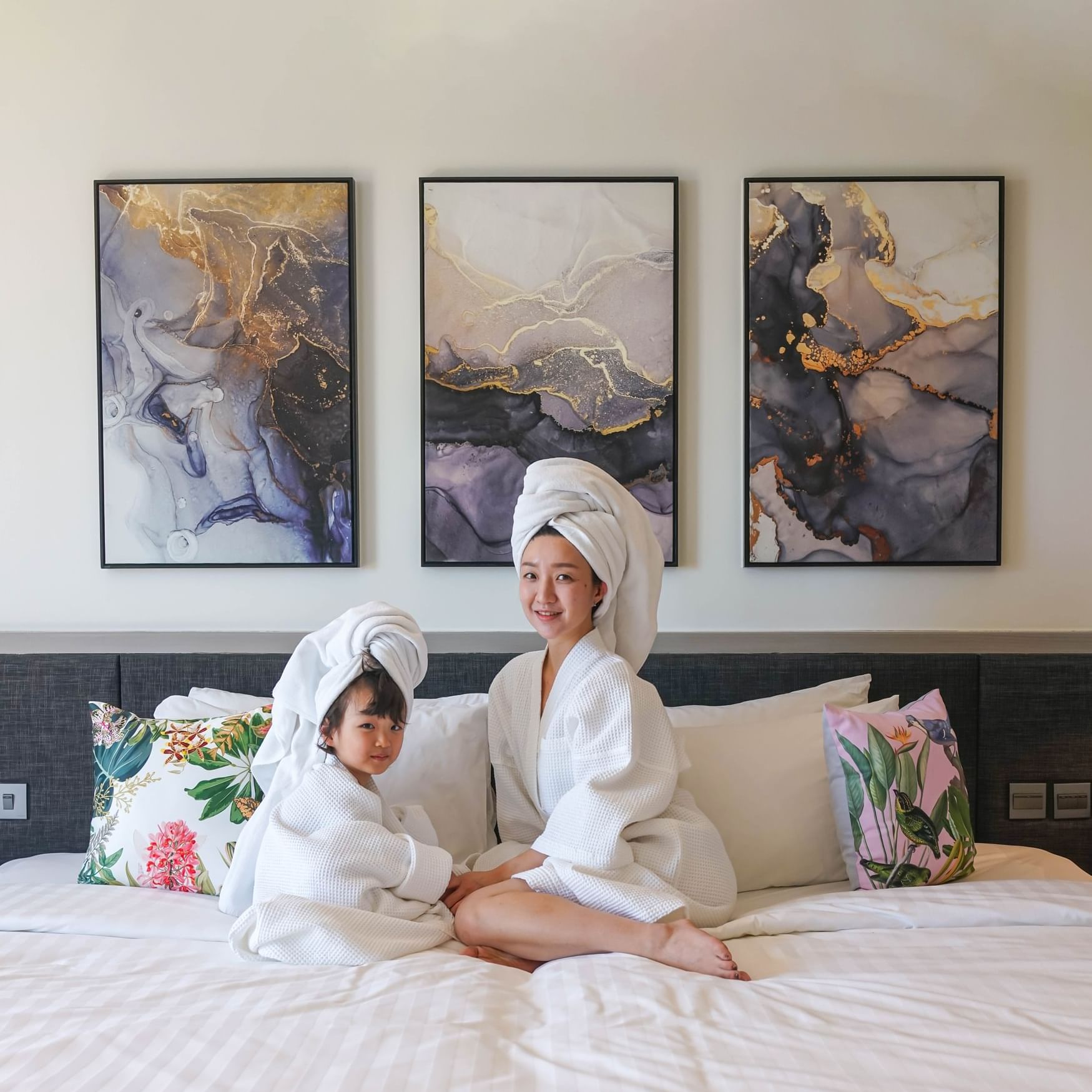 A mom and a child are smiling and sitting on bed and wearing the bathrobe