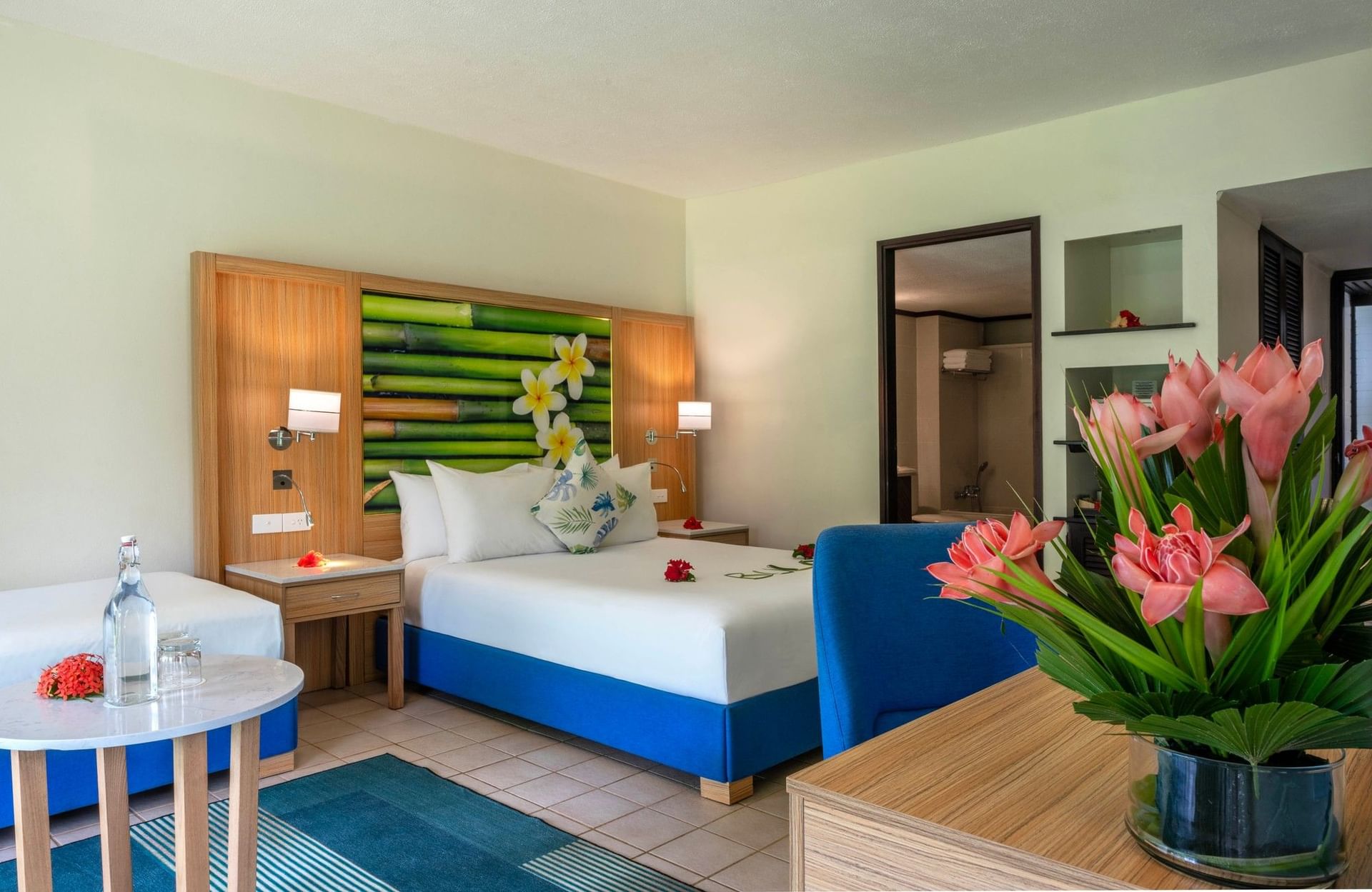 Water bottle on a table by a blue bed base under a bamboo mural in Superior Garden View Room at The Naviti Resort - Fiji