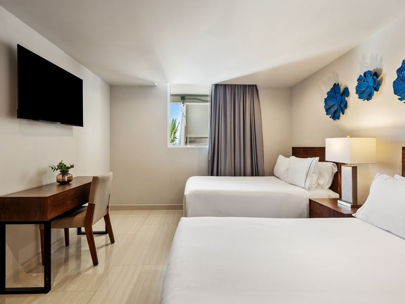 Penthouse room with two white beds, blue flower wall art, a TV, and a dark wooden desk at Sunvivia Mazatlán