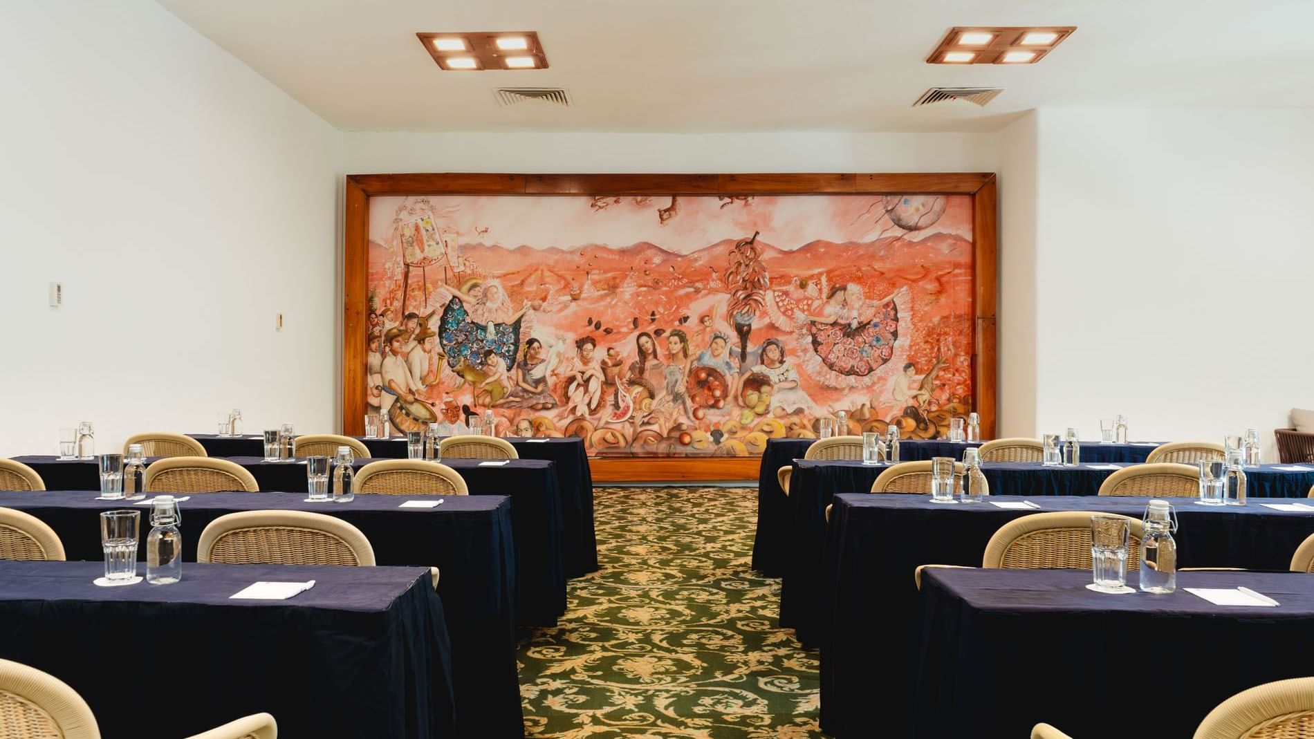 Classroom set-up in Indato II with carpeted floors and a vibrant mural on the wall at Camino Real Zaashila Huatulco