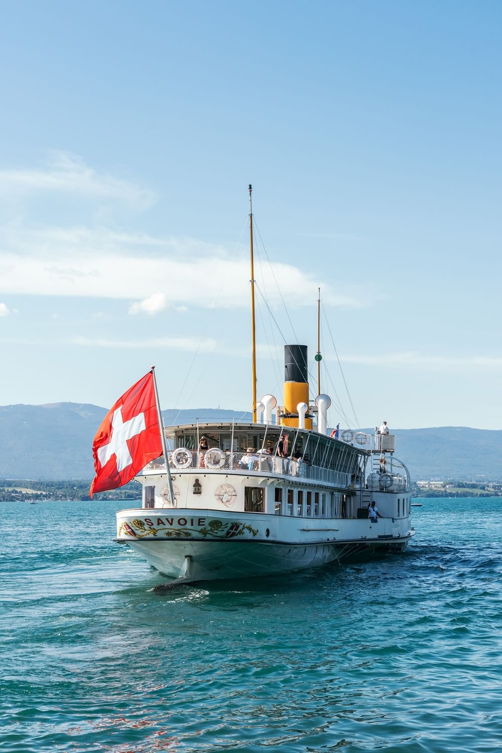 White Savoie steamboat with a red flag sailing on a blue lake under a clear sky near Warwick Geneva