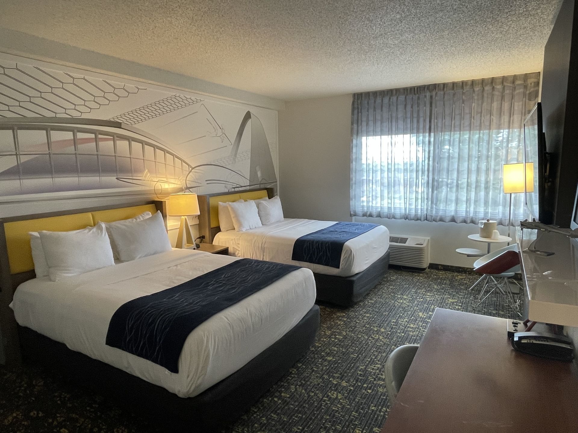 Two beds, TV, sitting area & workspace in Double Queen Standard at St. Louis Airport Hotel