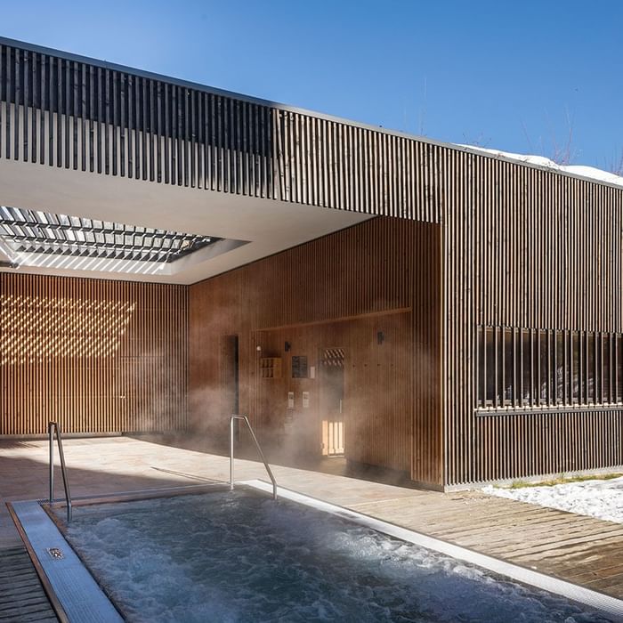 Outdoor thermal pool with steam rising from water at Falkensteiner Hotel Schladming