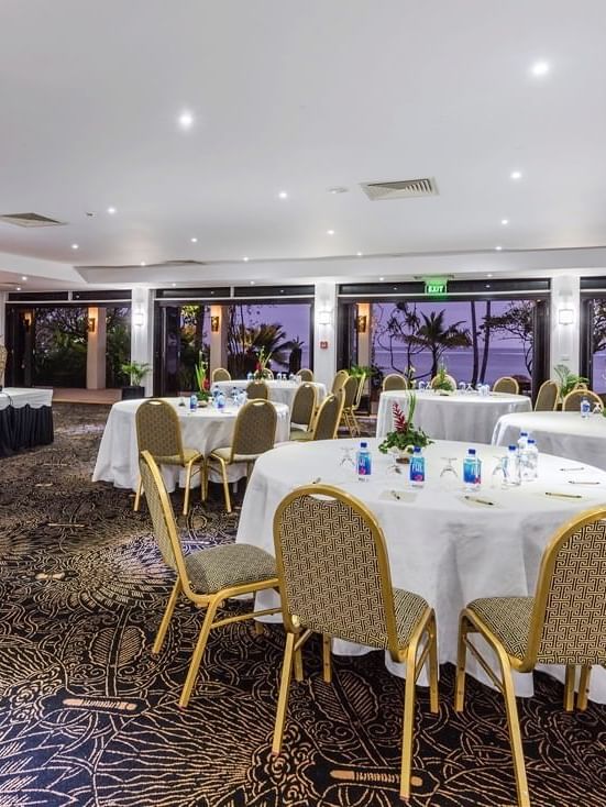 Coral Coast Conference Centre with round tables and chairs by glass doors at Warwick Fiji Resort and Spa