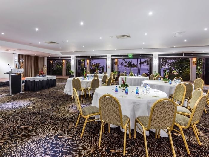 Coral Coast Conference Centre with round tables and chairs by glass doors at Warwick Fiji Resort and Spa