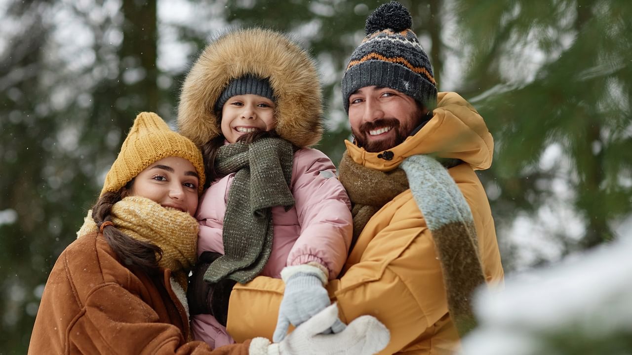 A family of four in winter clothes and scarves smiling and posing for a photo in the snow.