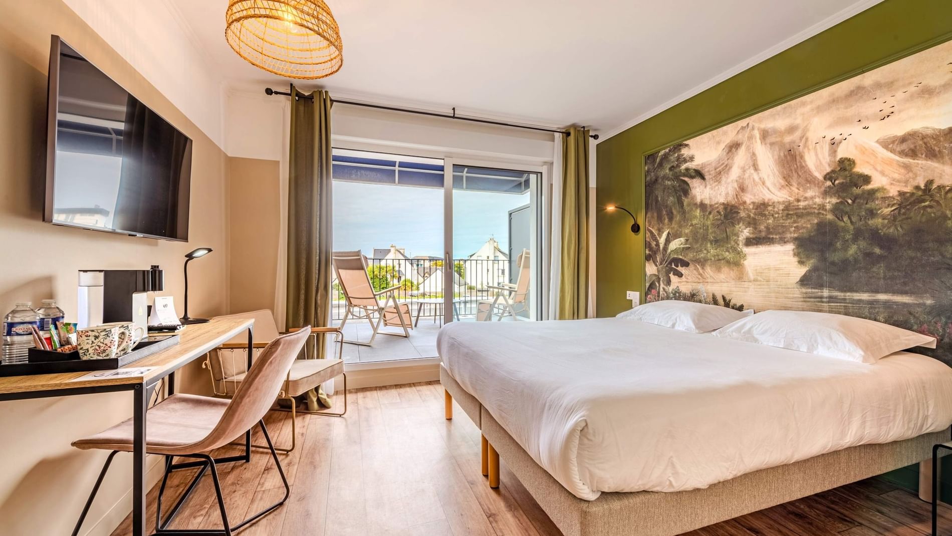 Double bed beside wooden desk with armchair near sliding glass door opening to balcony terrace at Hotel Spa Le Triton