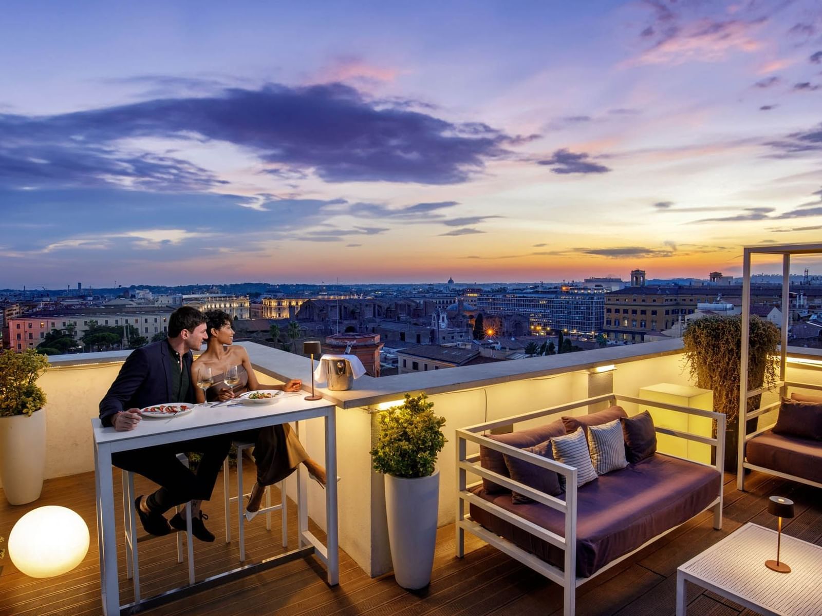 Couple enjoys a romantic dinner on Terrazza Cielo rooftop, with a vibrant city sunset at The Independent