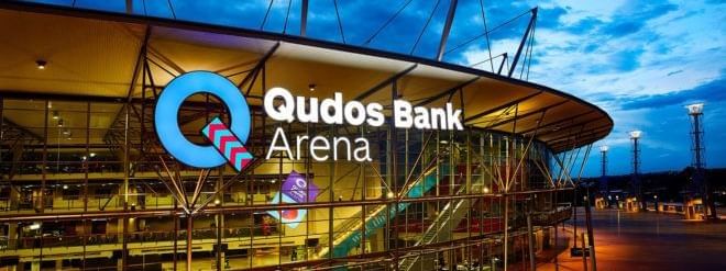 Exterior of Qudos Bank Arena with prominent illuminated signage at dusk near Novotel Sydney Olympic Park