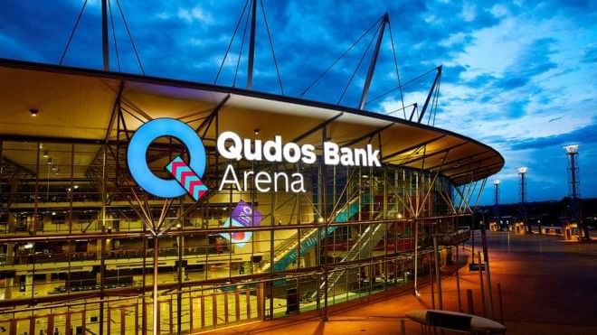 Exterior of Qudos Bank Arena with prominent illuminated signage at dusk near Novotel Sydney Olympic Park
