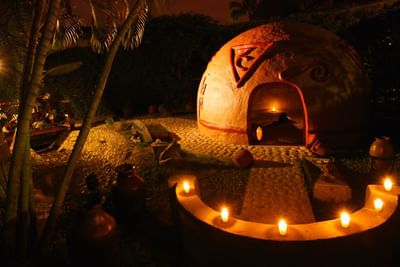 Night scene of a dome structure with lit candles and intricate designs, surrounded by tropical elements.