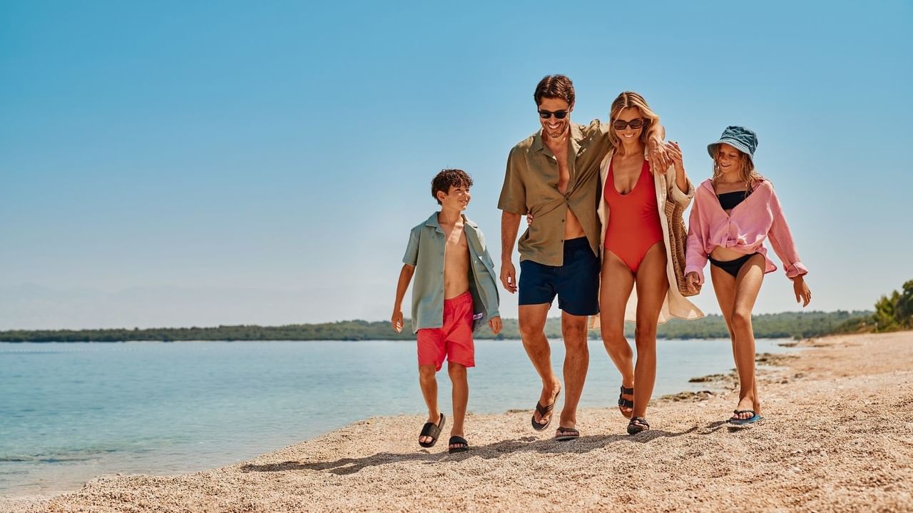 Famiglia di quattro persone, in abbigliamento da spiaggia, cammina sulla sabbia vicino all'acqua.