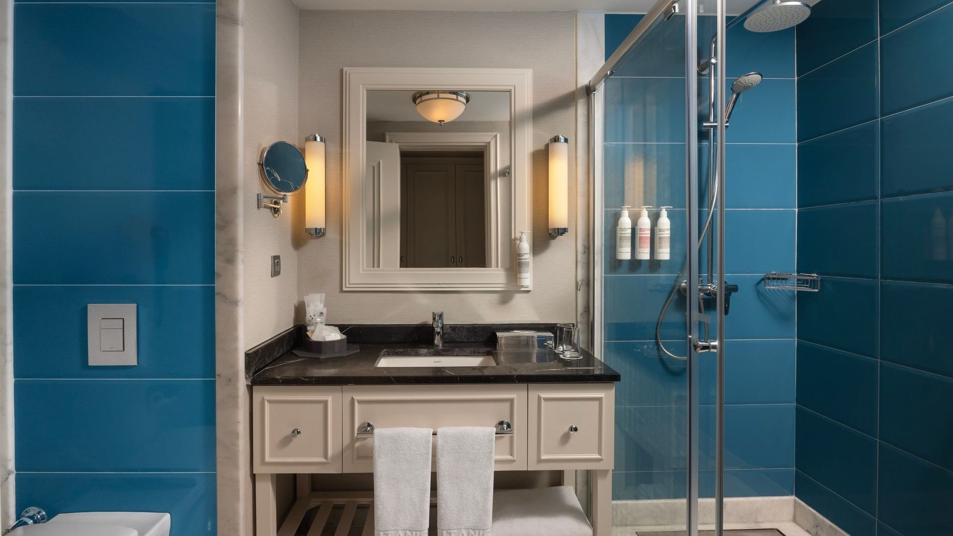 Riverside Room bathroom with teal tiles, white vanity, mirror, and glass-enclosed shower at Titanic Deluxe Golf Belek.