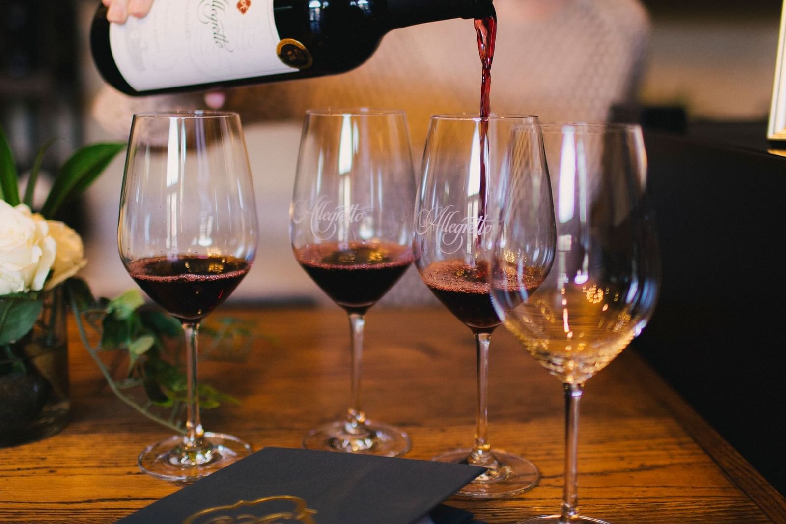 Four wine glasses lined up.  Woman pouring red wine.