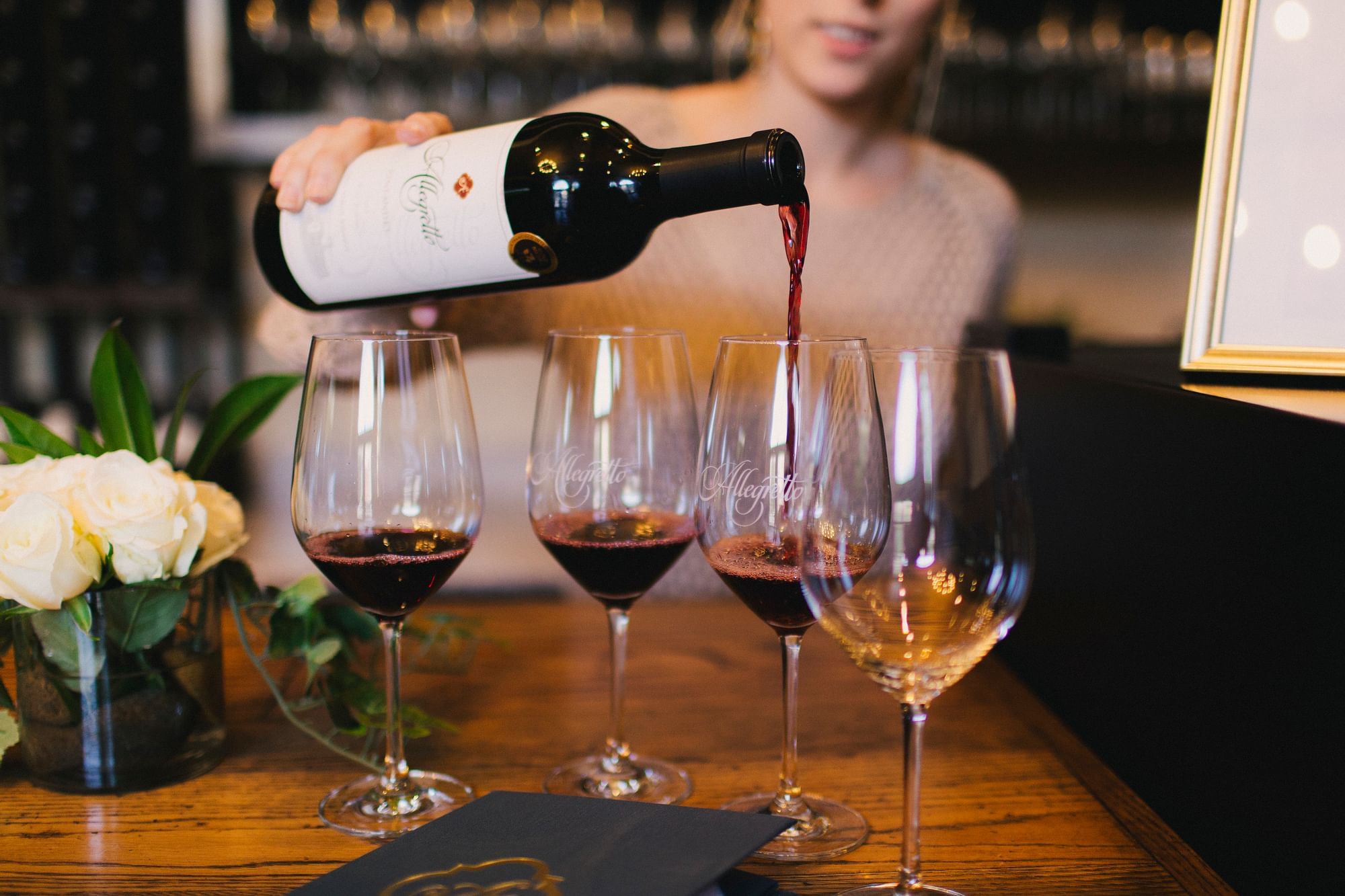 Four wine glasses lined up. Woman pouring red wine.