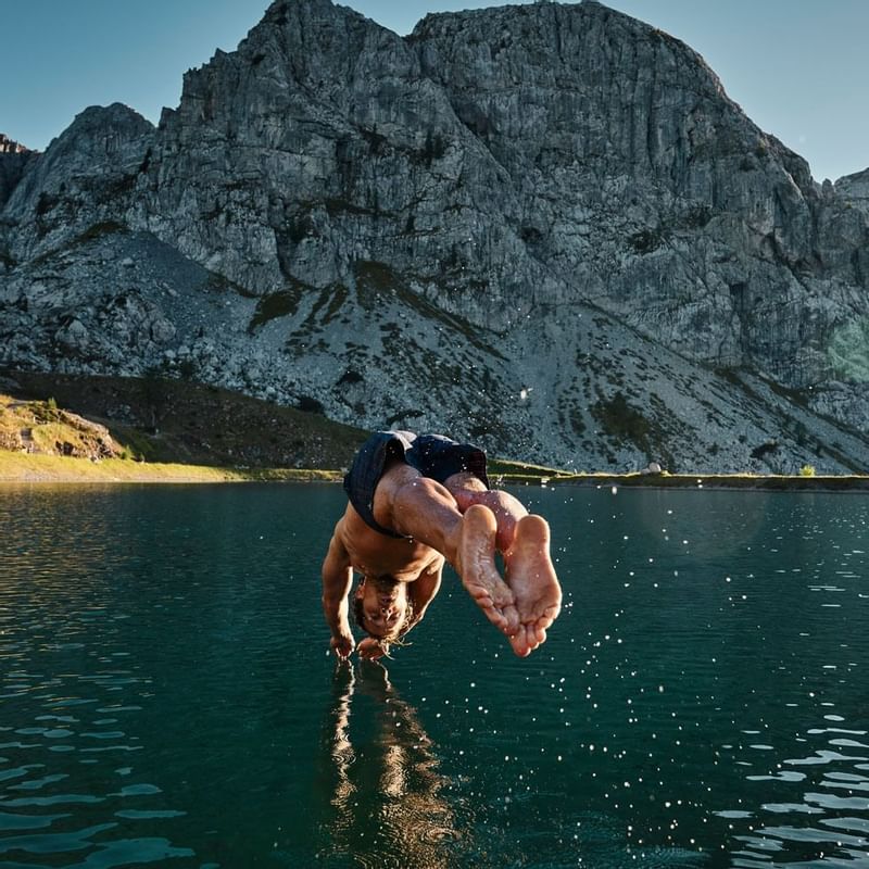 Man jumping to a river by mountains near Falkensteiner Hotels