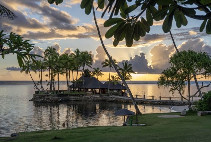 Sunset view of ocean, beach, and resort with tropical trees and thatched-roof structures at Warwick Fiji Resort and Spa.
