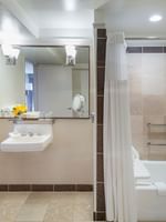 Bright bathroom with yellow flowers by a white sink under a large mirror in Accessible Deluxe Rooms at Warwick Denver