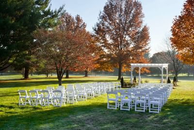 Outdoor event space at the Bolger Center set up with white chairs and a beautiful arbor surrounded by trees
