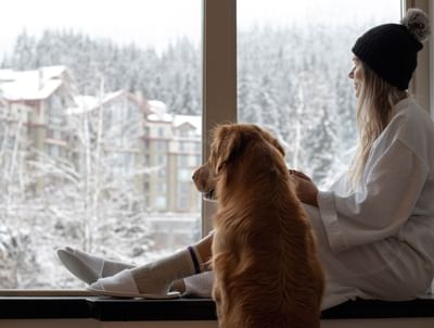 Lady with a dog looking through a window at Aava Whistler Hotel