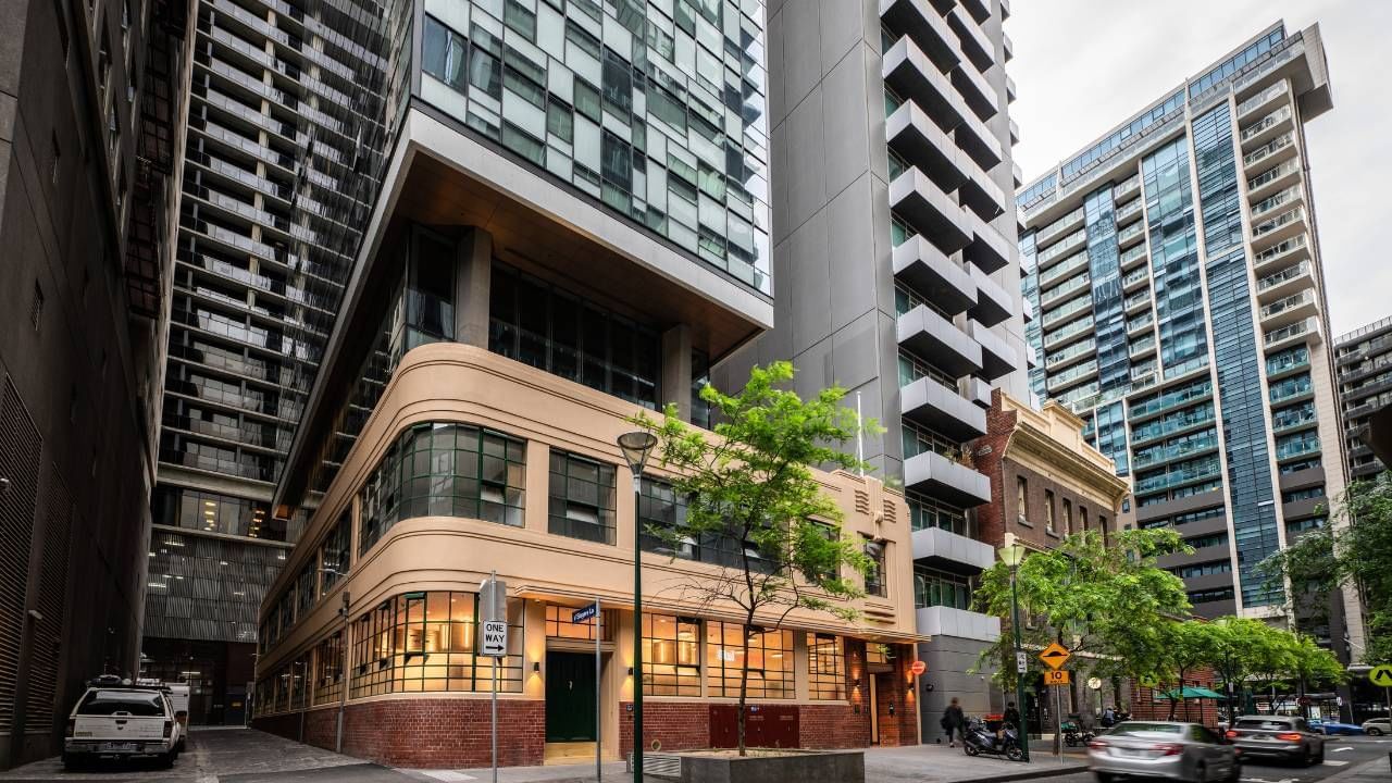 Modern buildings and skyscrapers in an urban area with cars, trees, and a narrow street.