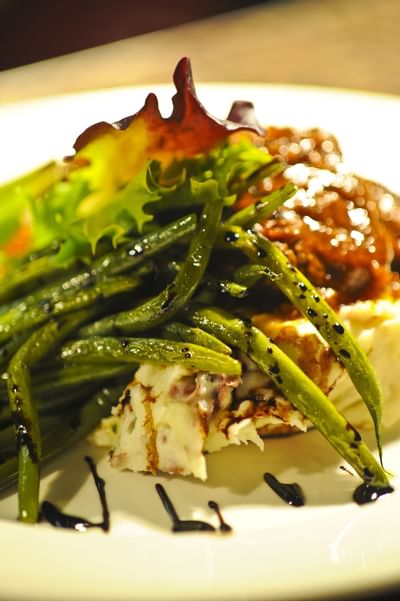 Plated meal with green beans, mashed potatoes, and meat drizzled with sauce at Farmington Inn and Suites