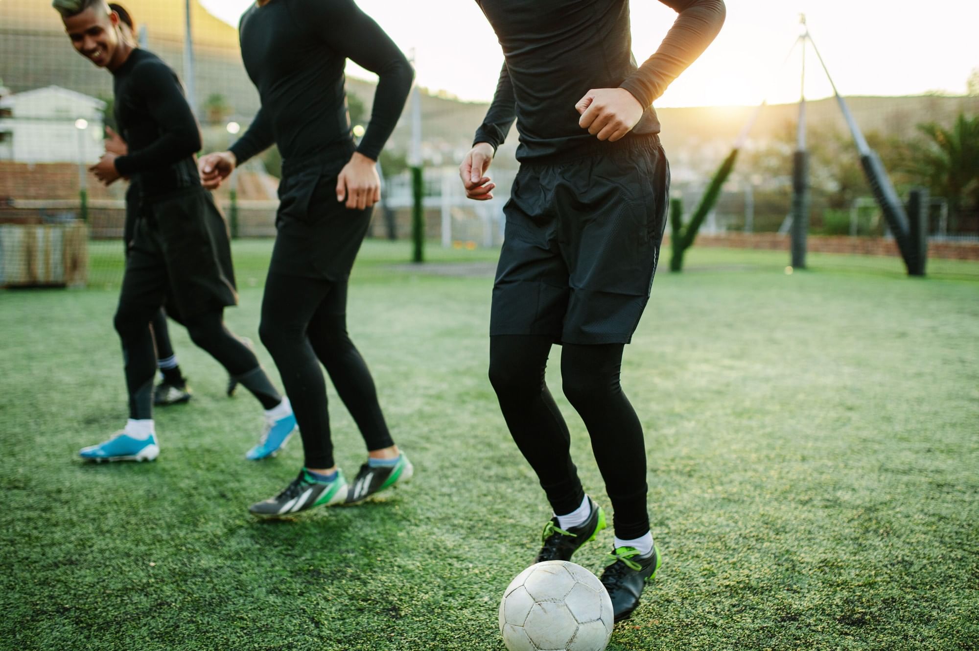 Men running across an outdoor turf field during football practice at dusk beside the fitness club at Village Hotel Sheffield