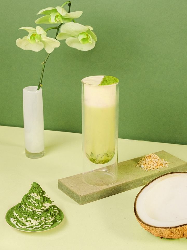 Glass of coconut matcha milk tea served with coconut shell, powdered matcha, & orchid in Park Lounge at Park Hyatt Saigon