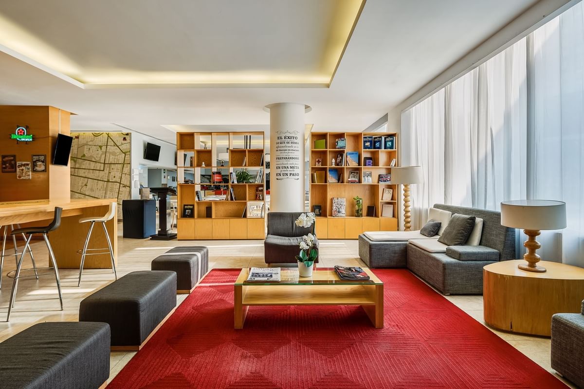 Área de lounge del lobby luminosa y acogedora con alfombra roja y grandes estanterías en Fiesta Inn