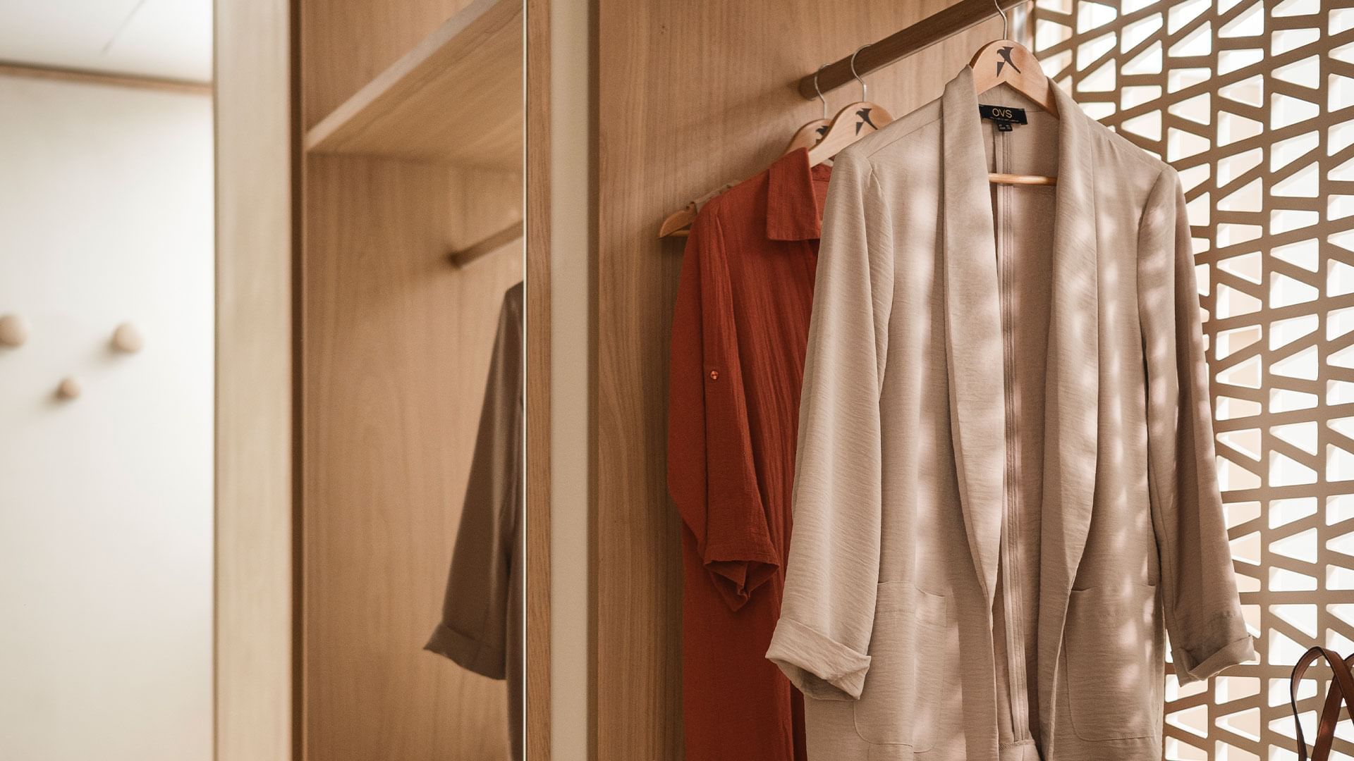 Three clothes hanging on hangers in front of a wooden door and mirror.