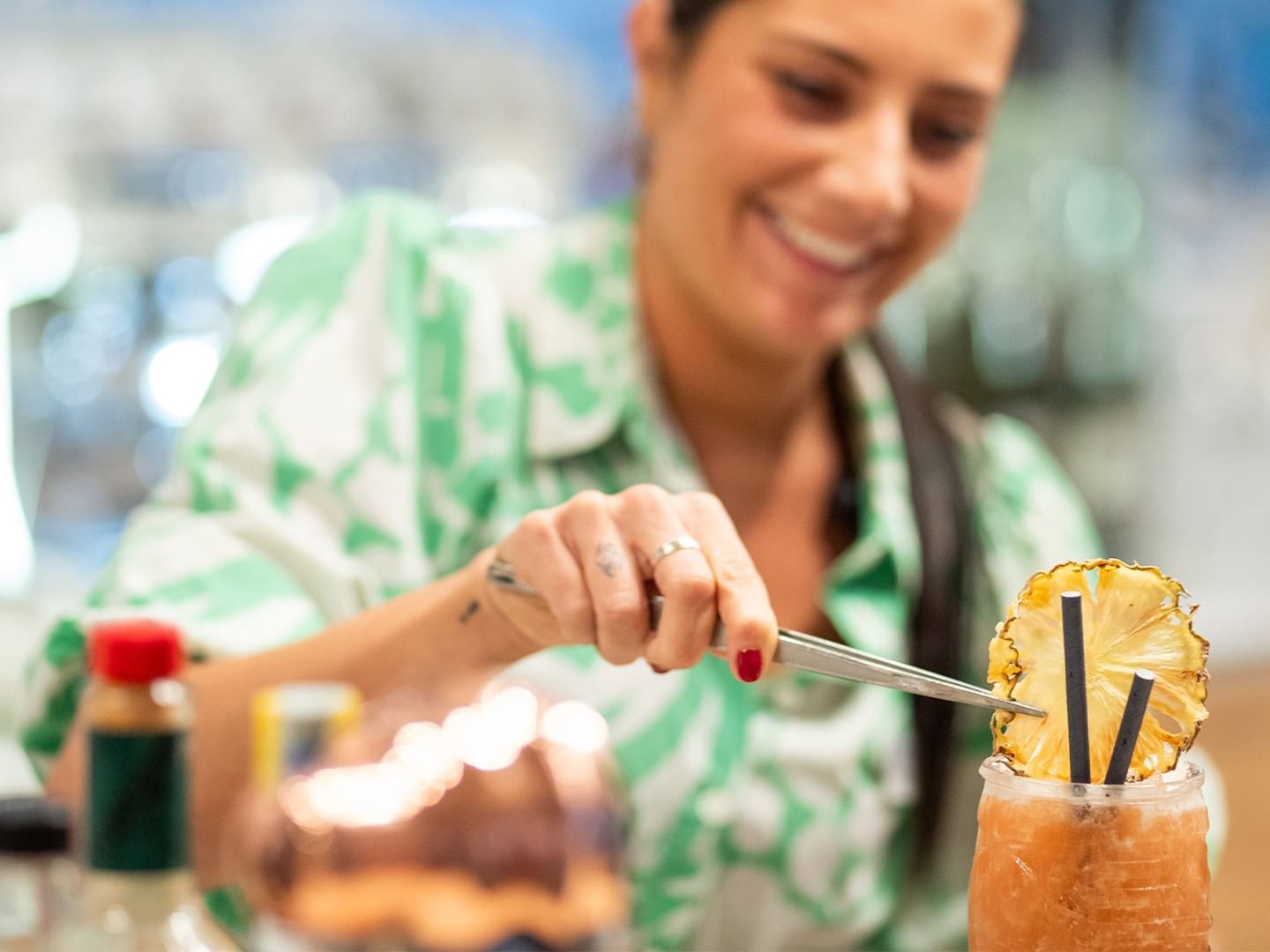 Frau mit grünem Shirt mischt einen Cocktail mit Ananasstück und Strohhalm.