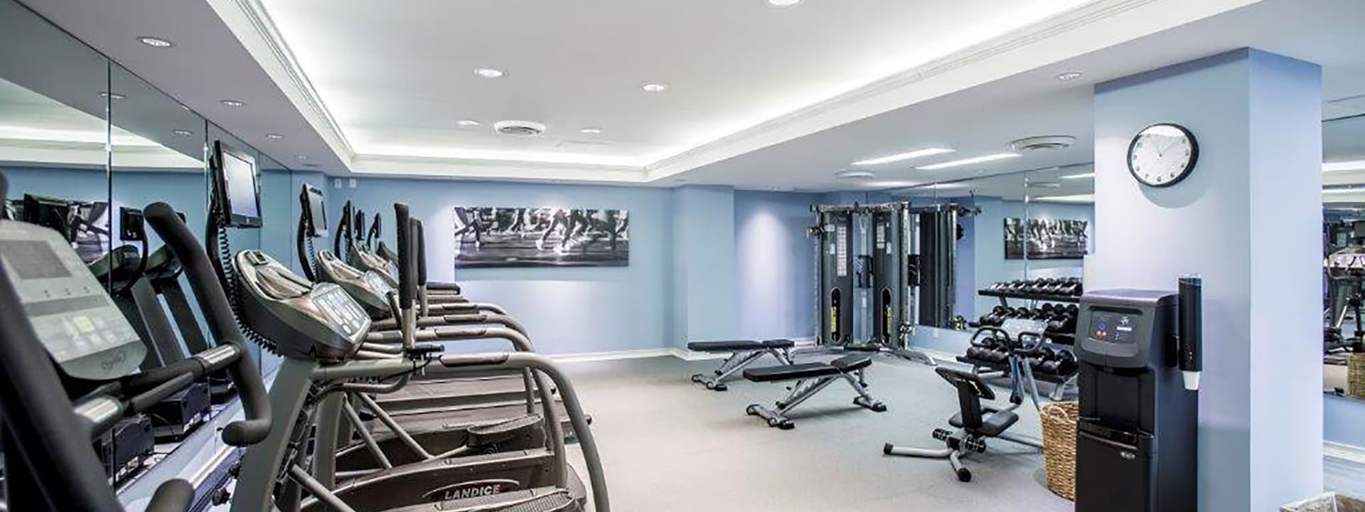 Treadmills by weight benches under bright lights in the modern fitness center at Warwick Melrose Dallas