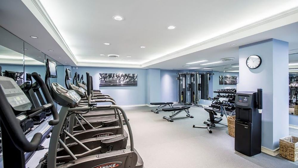 Treadmills by weight benches under bright lights in the modern fitness center at Warwick Melrose Dallas