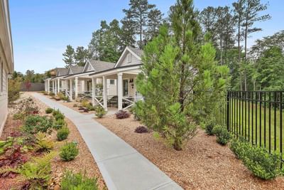 Charming cottages line with wide porches, garden views, and a paved path under a blue sky by Cottages at Laurel Brooke