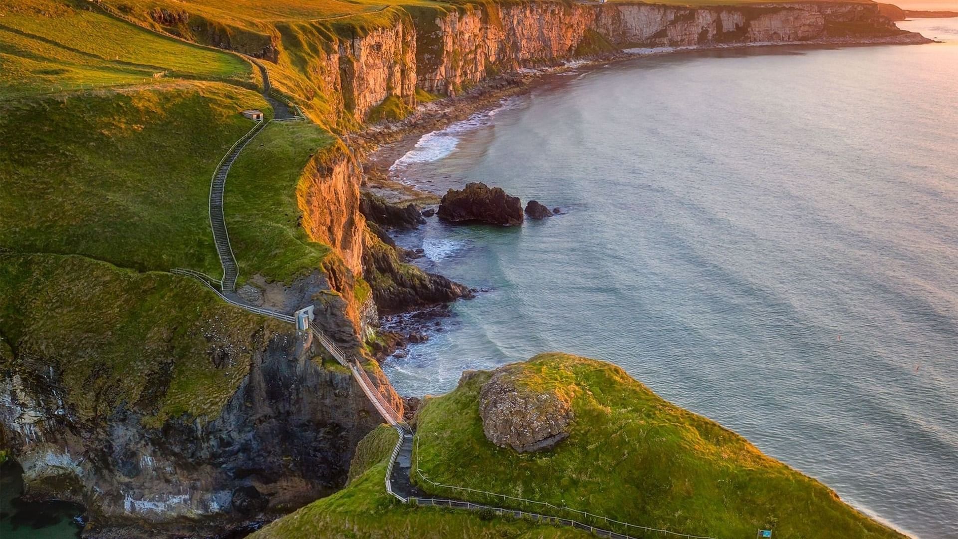 Stunning coastal cliffs with a winding path, green hills and ocean waves at sunset in Bally Castle near Dunluce Lodge