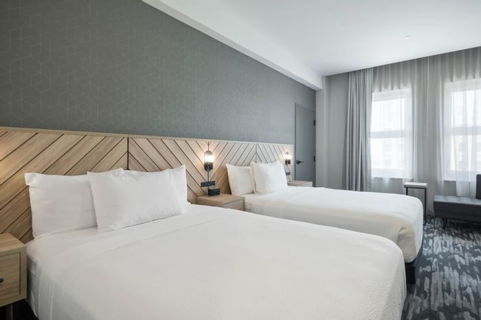 fort worth hotel room with 2 queen beds with a wooden headboard in chevron pattern, light grey walls and white ceiling