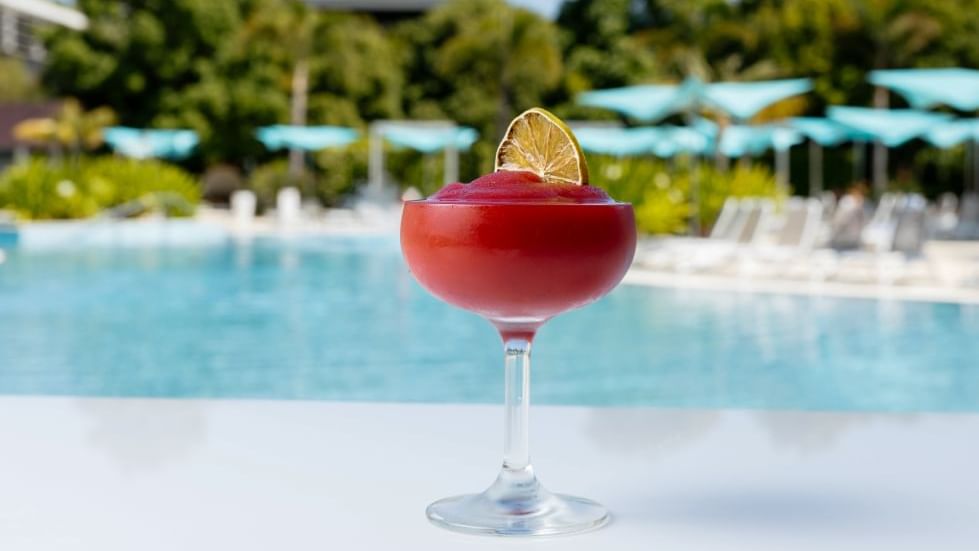 Close-up of red cocktail with a lime garnish by a pool at Crown Hotels