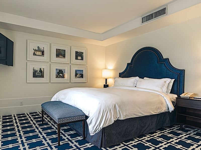 A comfortable guest room at El Prado Hotel, featuring a large bed with a blue headboard and framed artwork