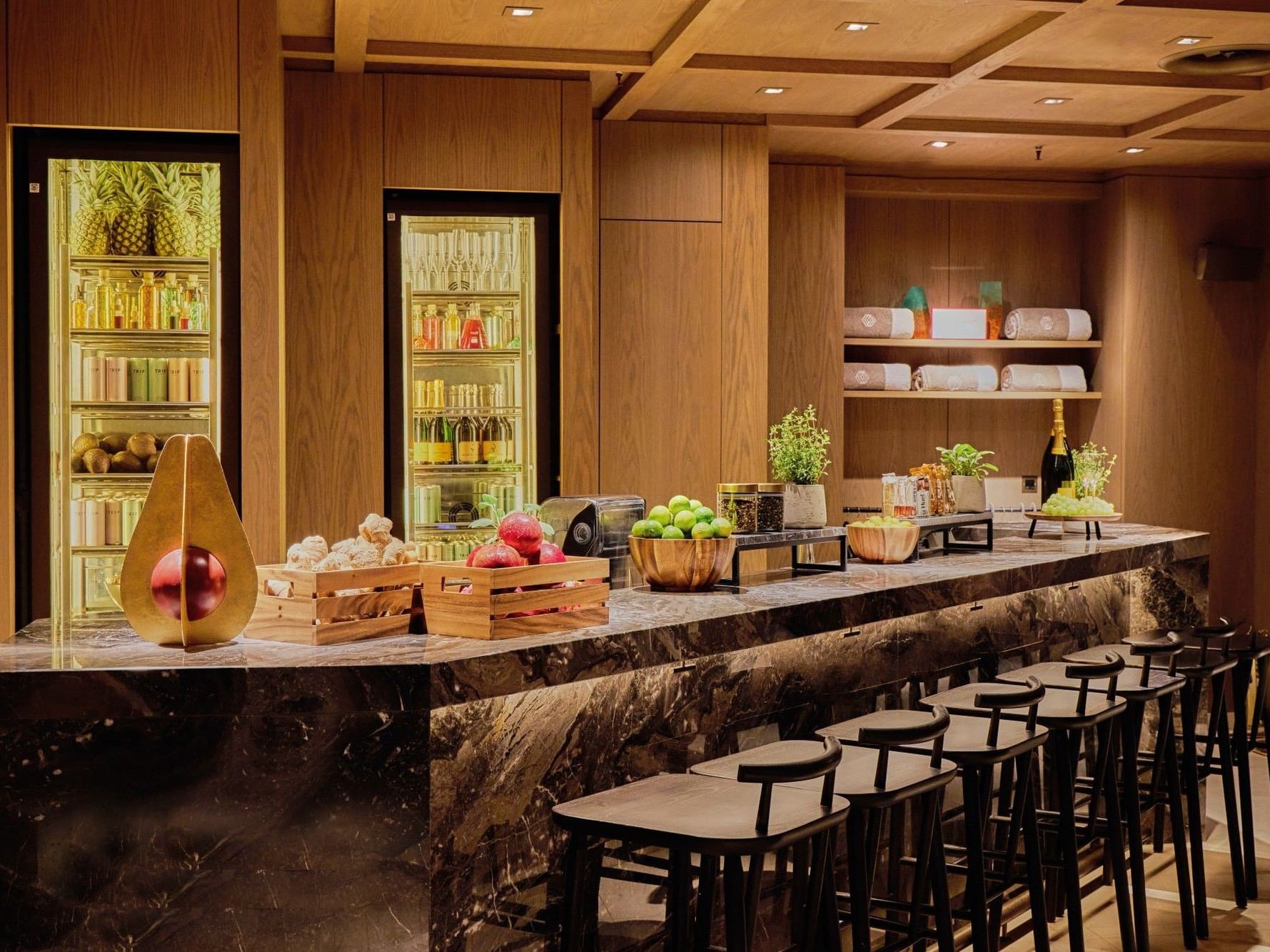 Refuel Bar with marble counter, black stools, and illuminated beverage displays at The Londoner Hotel
