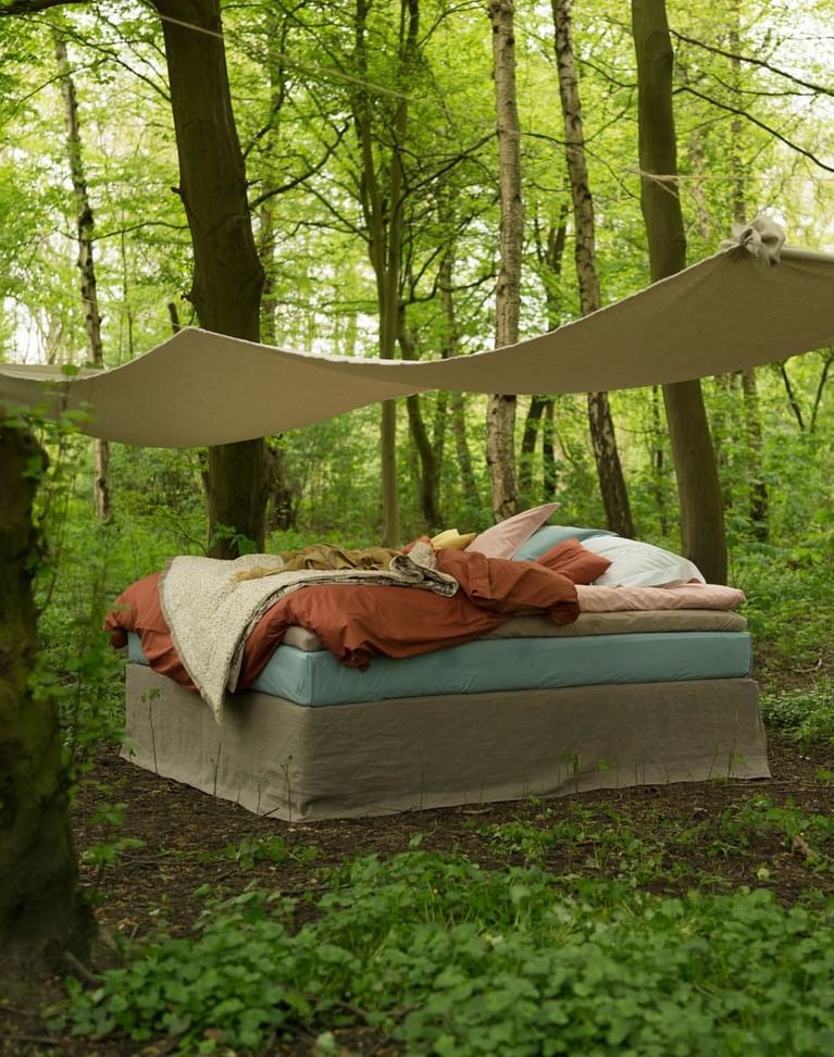Cozy bed setup in a forest, shaded by a canvas and surrounded by trees near Avaneo Hotel, highlighting hotel sustainability