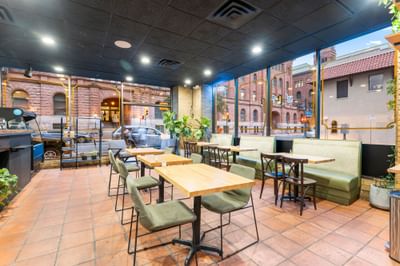 Bright Coffee Bar interior at The Riverwalk Plaza Hotel with wooden tables and large windows overlooking a scenic urban view