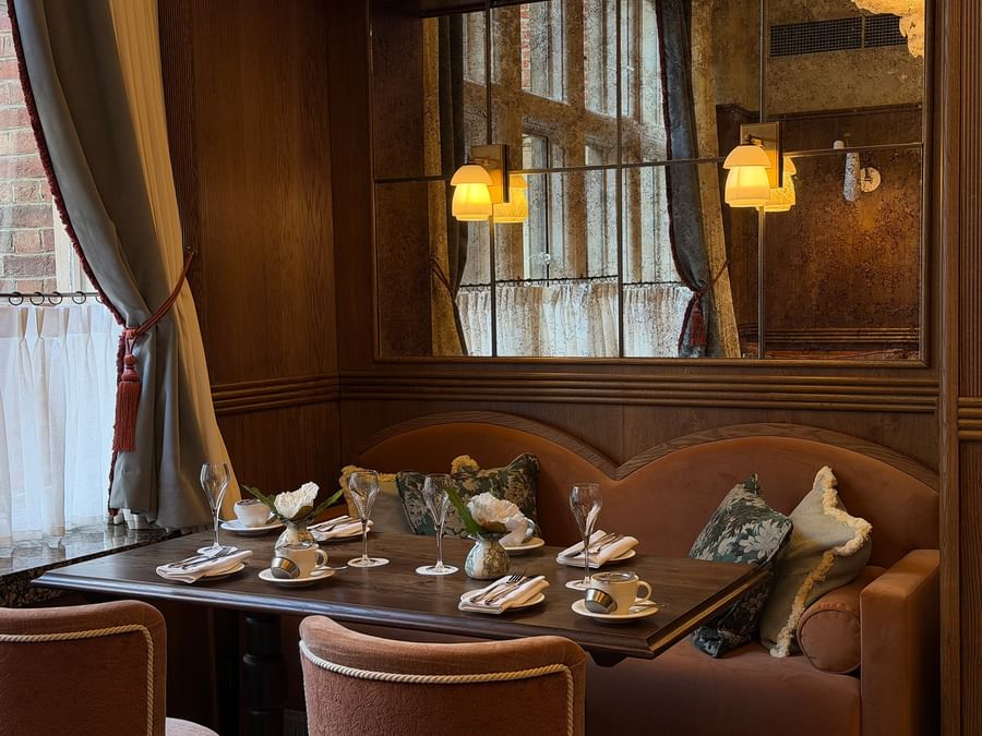Dining table with plush chairs set by a wood-paneled wall and mirrors at The Capital Hotel, Apartments and Townhouse