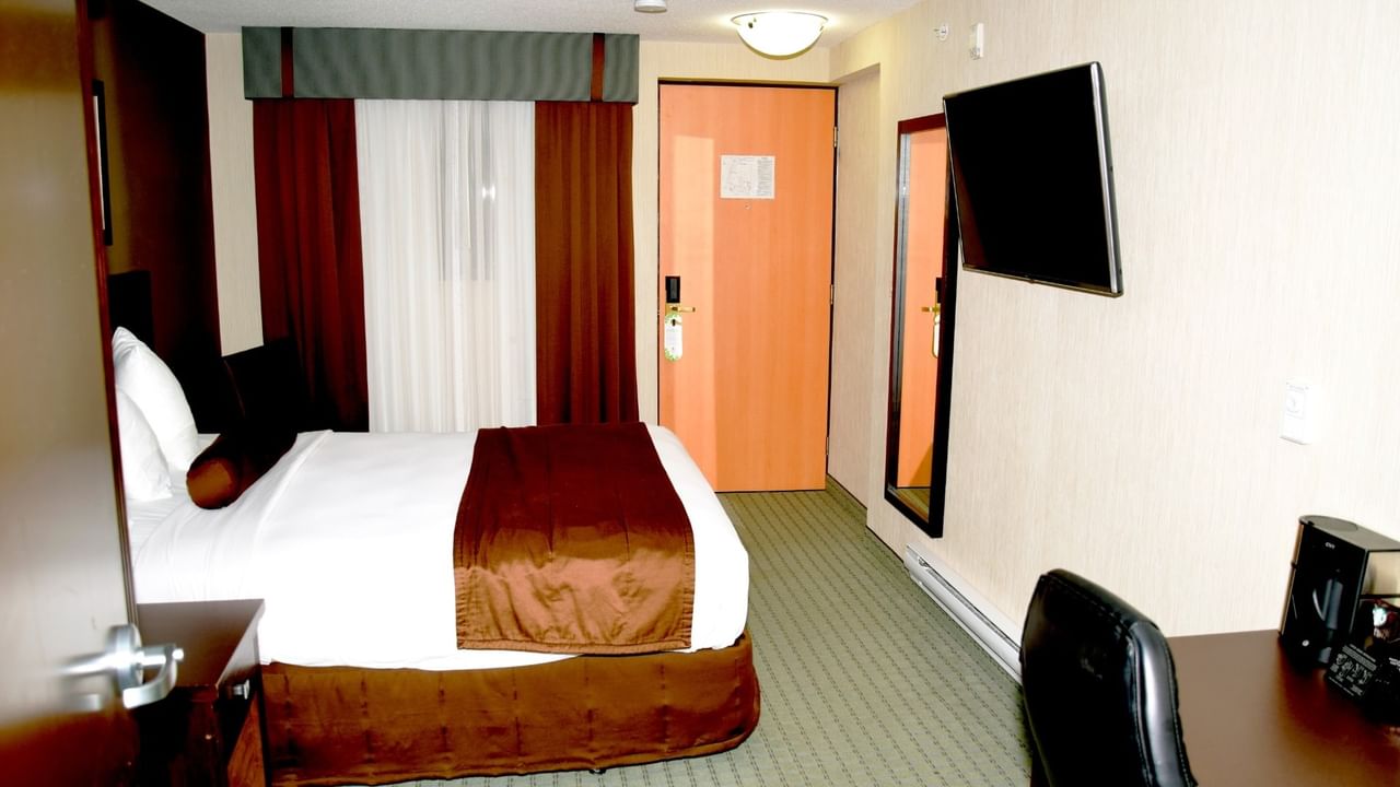 An accessible hotel room with a bed and wall-mounted TV.