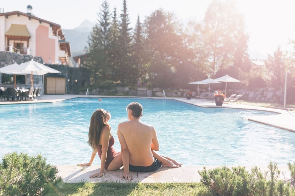 A couple seated on the edge of the outdoor pool at Liebes Rot