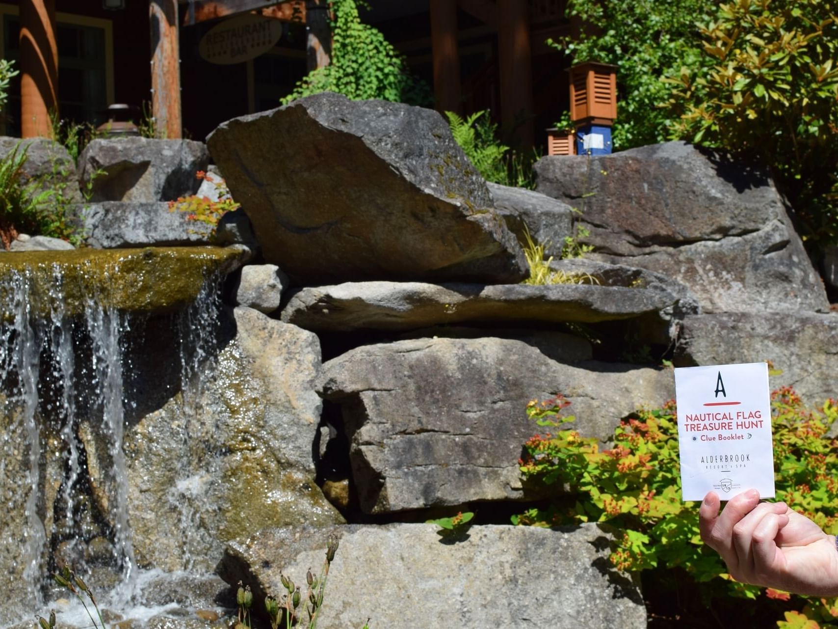 Hand holding a Nautical Flag Scavenger Hunt event card by a water stream near Alderbrook Resort & Spa