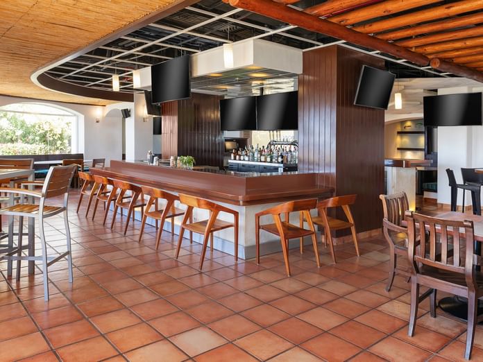 Sports Bar with wooden barstools, a terra cotta tiled floor, and TV screens at Hacienda del Mar Los Cabos