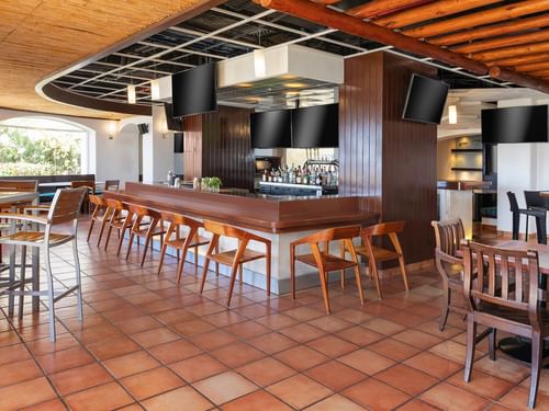 Bar deportivo con taburetes de madera, suelo de terracota y pantallas de televisión en Hacienda del Mar Los Cabos