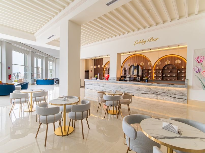 Lobby Bar with tables, chairs, and a marble countertop, framed by large windows and a floral painting.