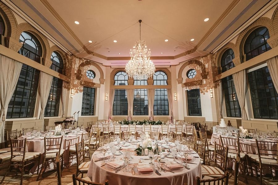 Grand ballroom with an ornate chandelier, arched windows, and dining tables set for a wedding at Warwick Allerton Chicago